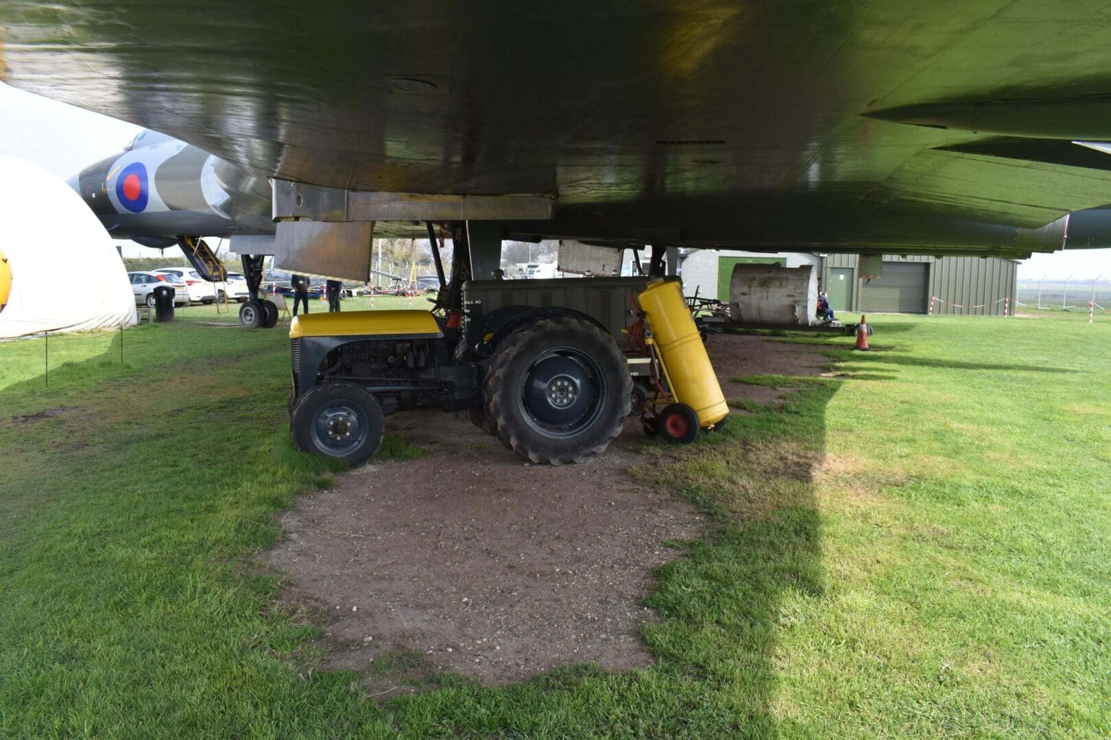 Tractor parked under large aircraft wing.