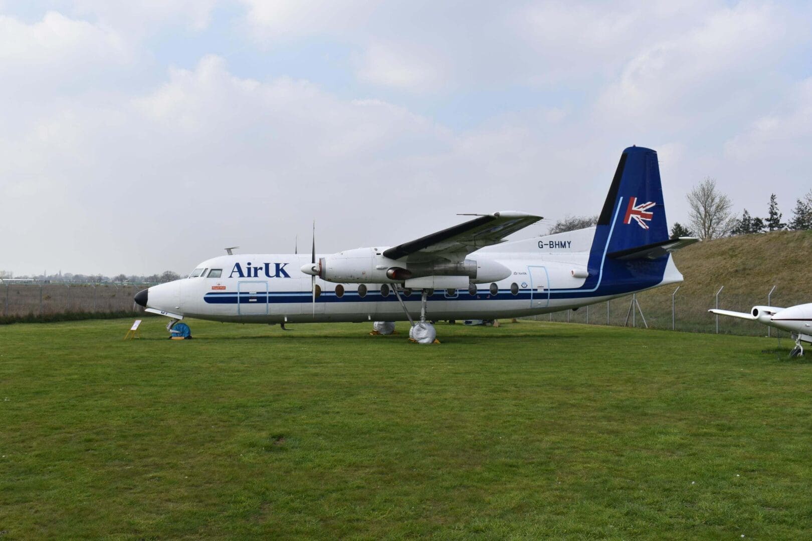 Airplane parked on grassy field, cloudy sky.