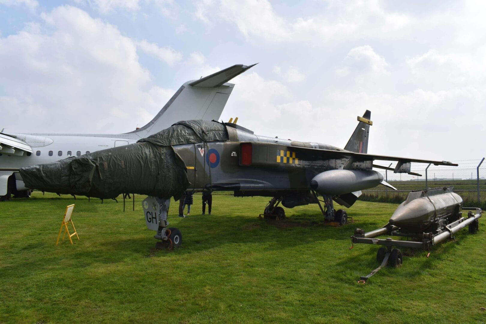 Covered military aircraft displayed on grassy field.