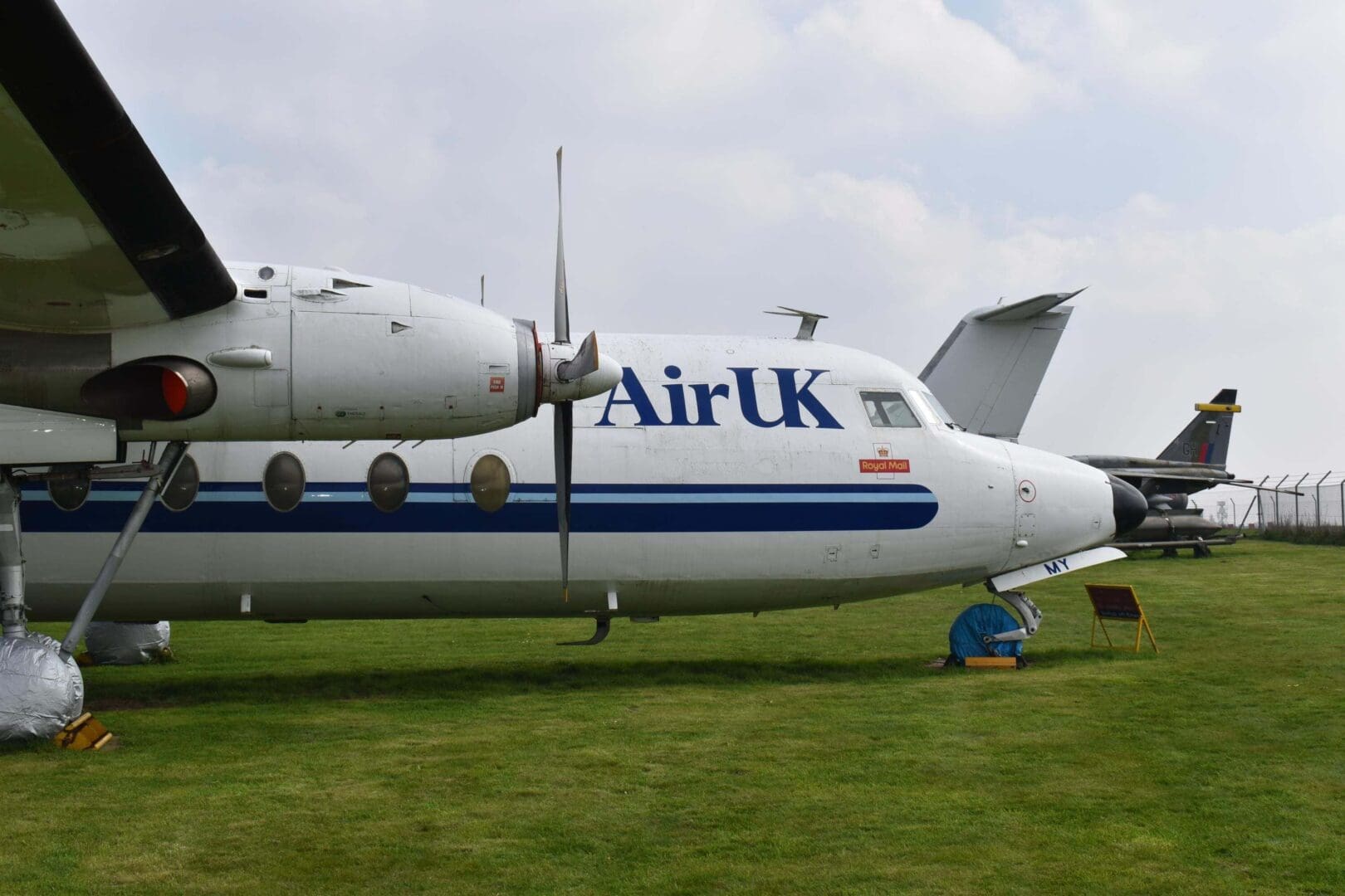 Airplane parked on grassy airfield under clouds.