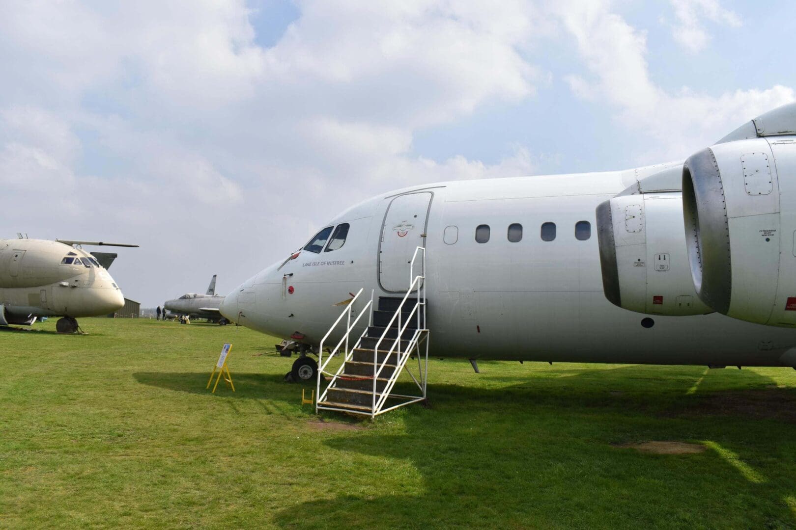 Parked airplanes on grassy field under clouds.