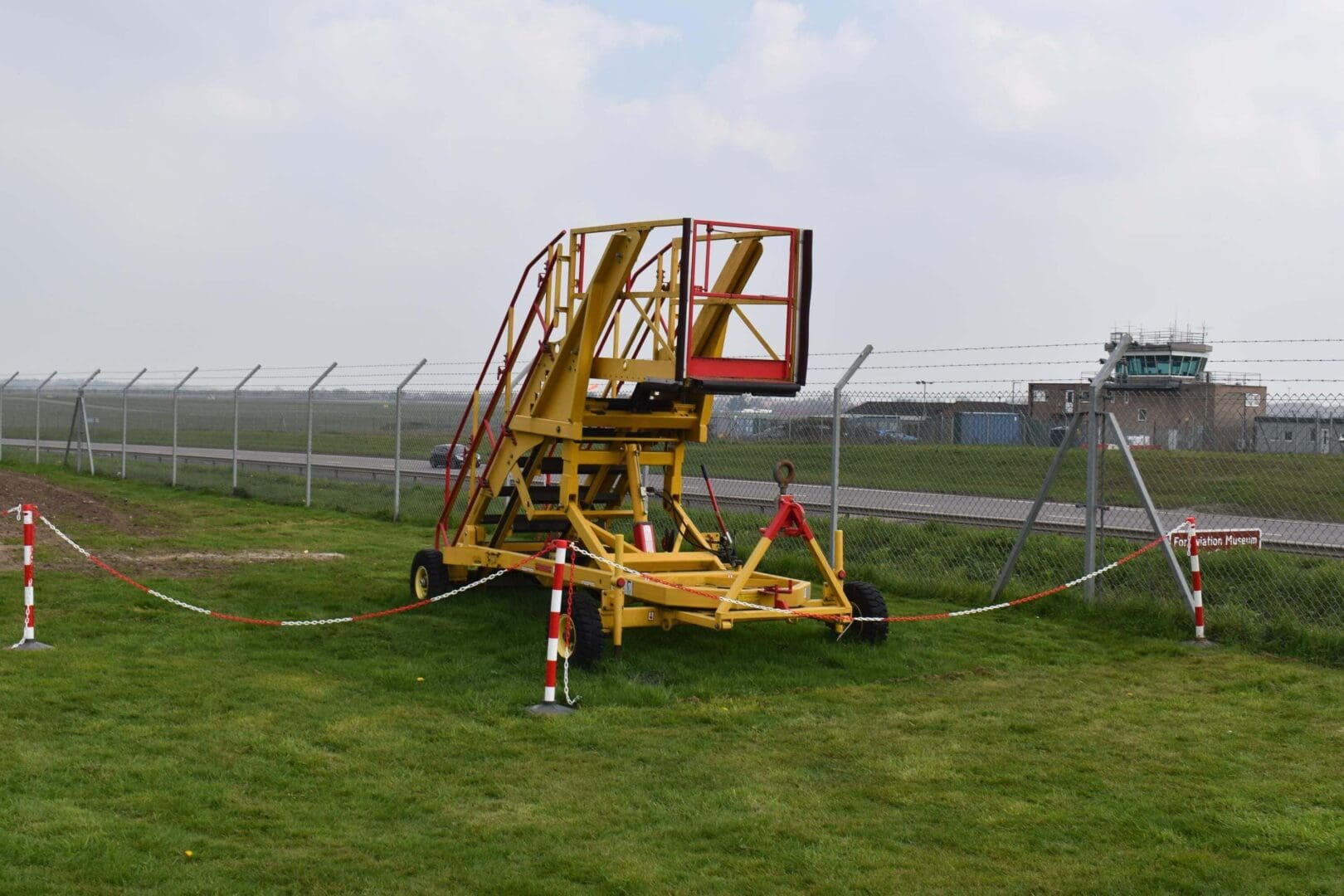 Yellow aircraft maintenance platform by airport fence.