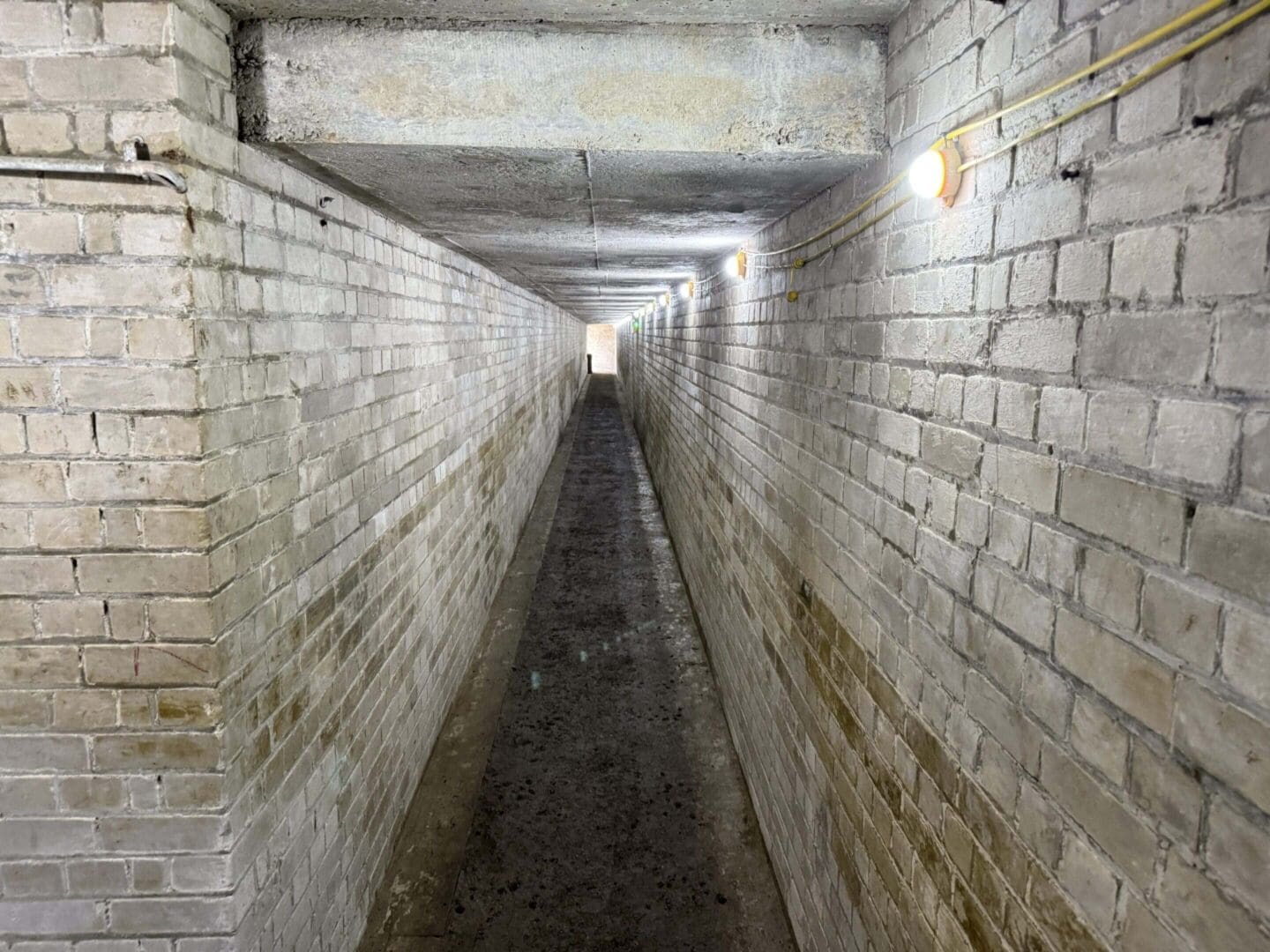 Narrow brick corridor with overhead lights.