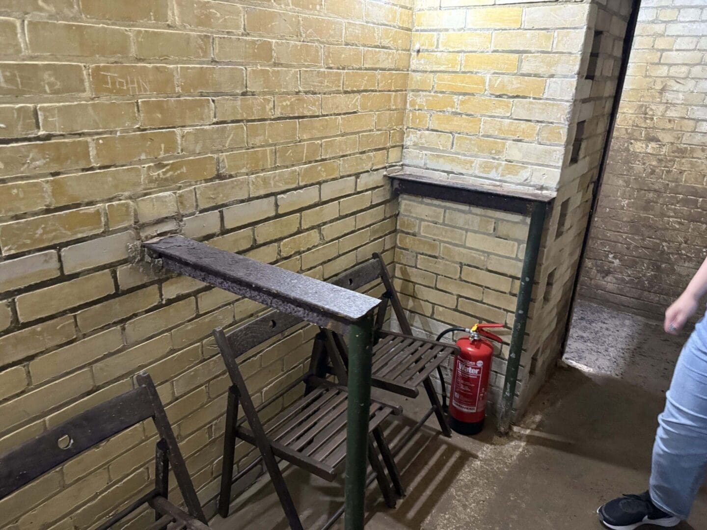 Narrow brick room with folding chairs and extinguisher.