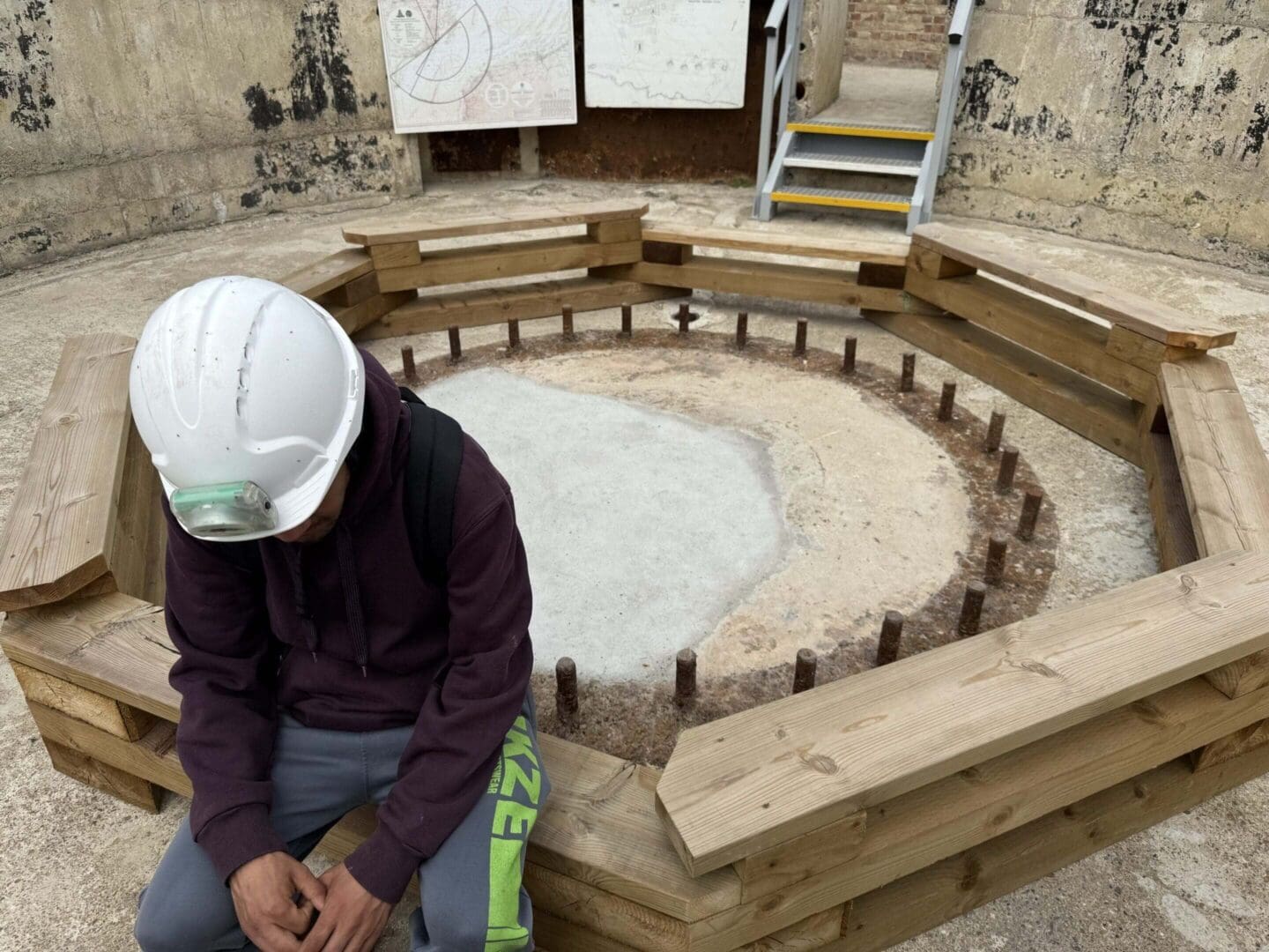 Person in hard hat sitting near foundation.