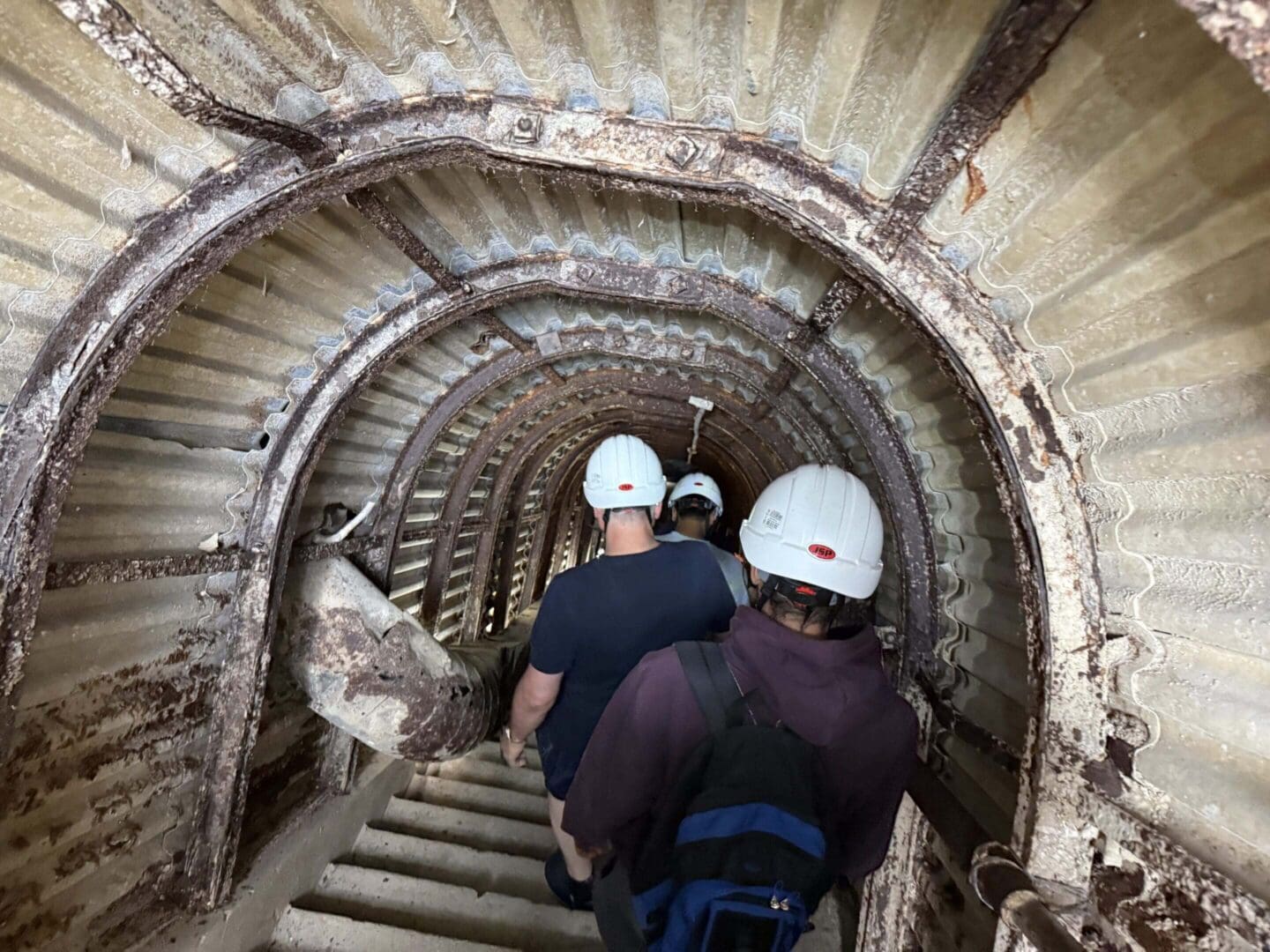 People walking in a corrugated metal tunnel.
