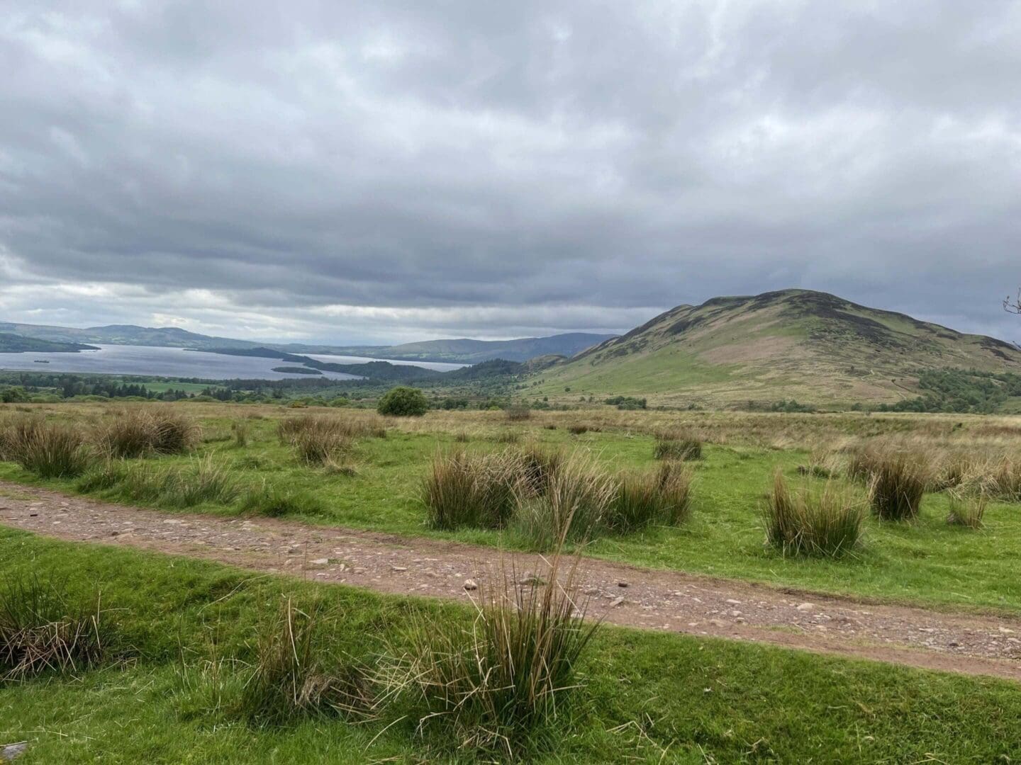 Cloudy landscape with grassy hills and path.