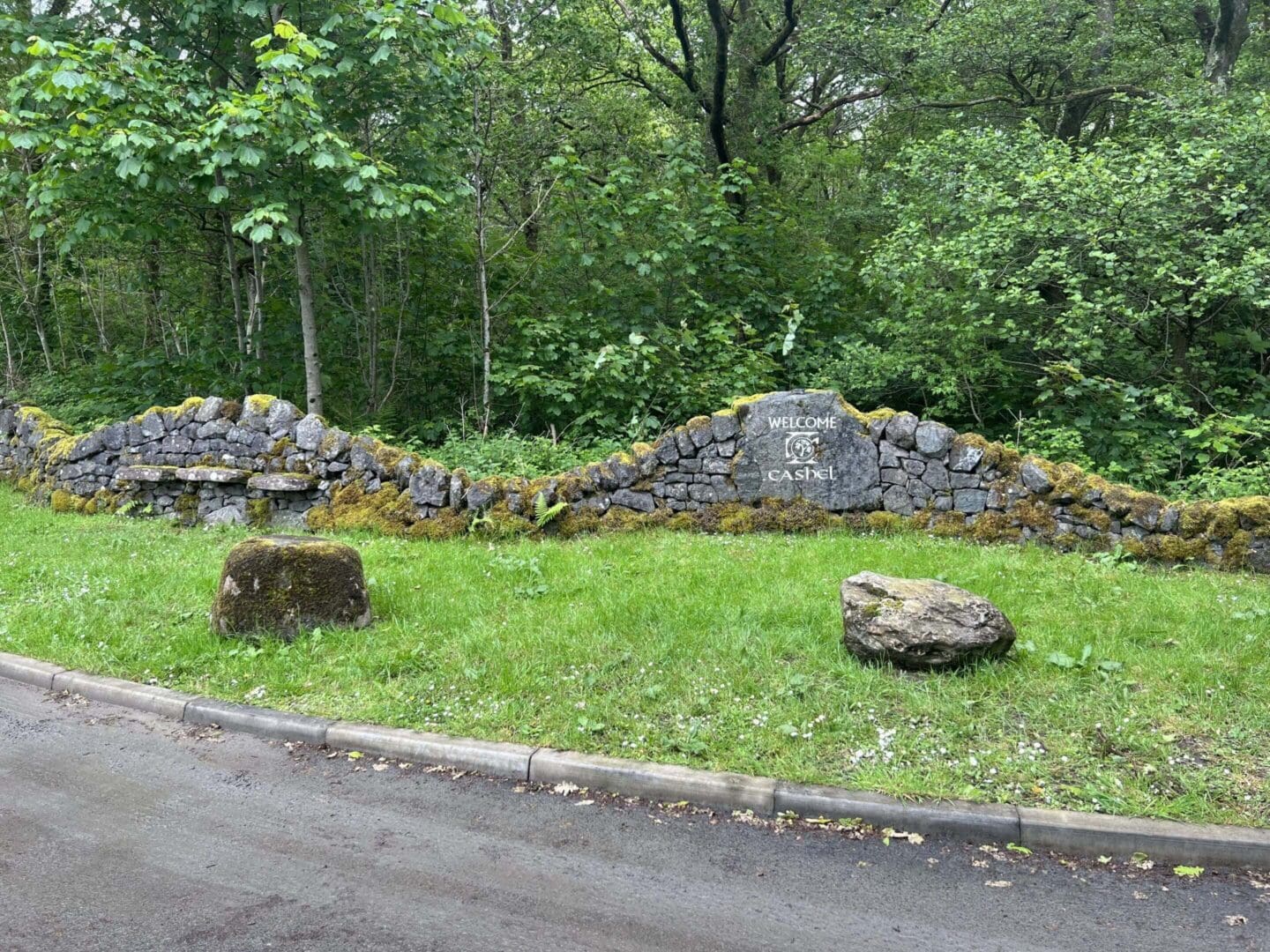 Stone wall with welcome sign and greenery.