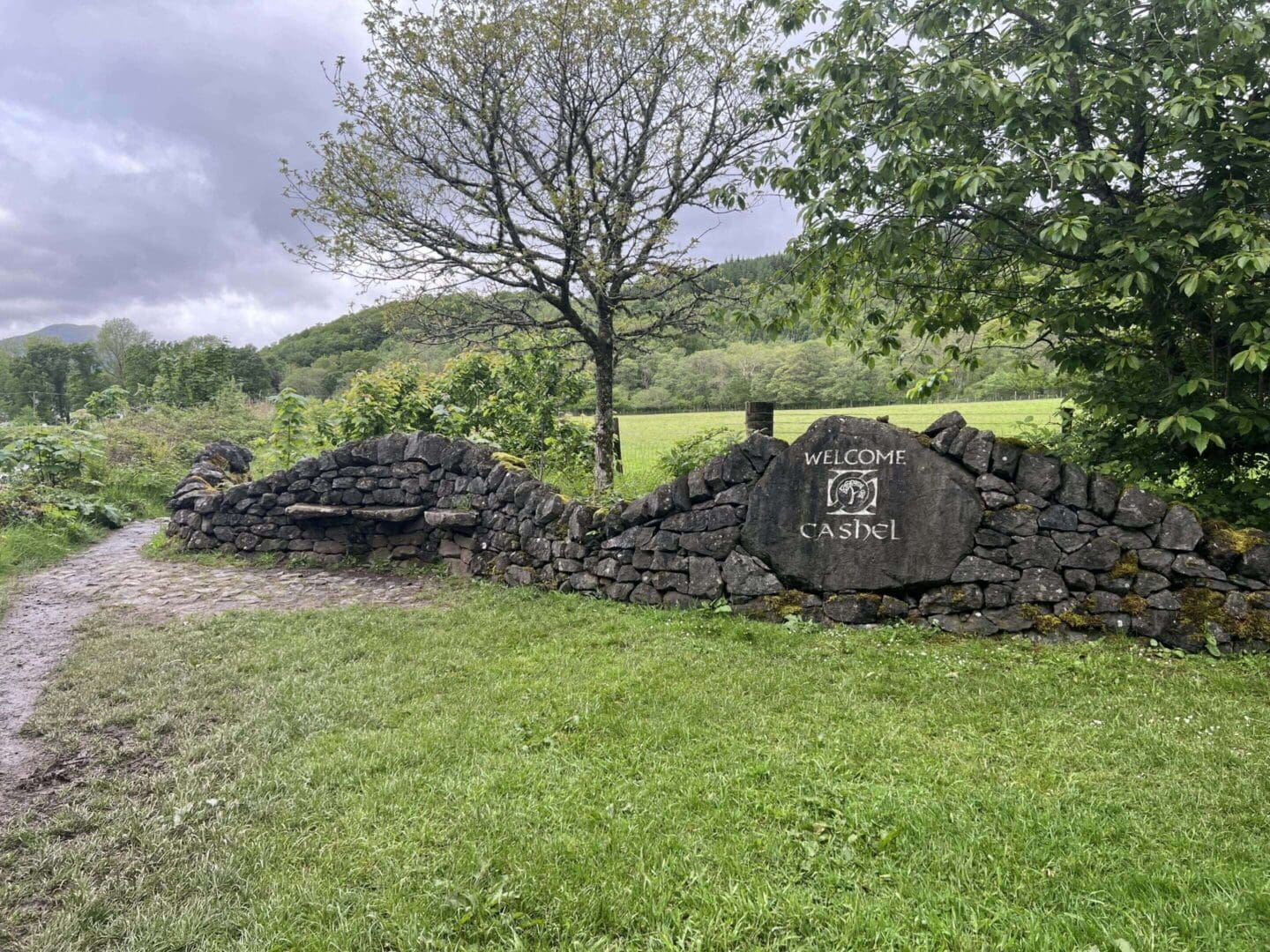 Stone welcome sign on a grassy path.