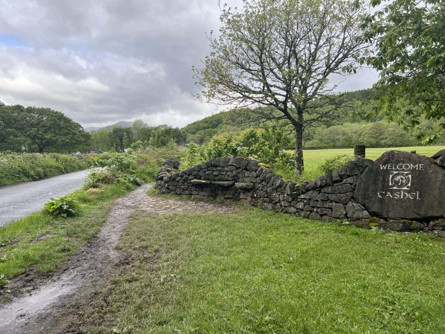 Welcome sign and stone wall on path.